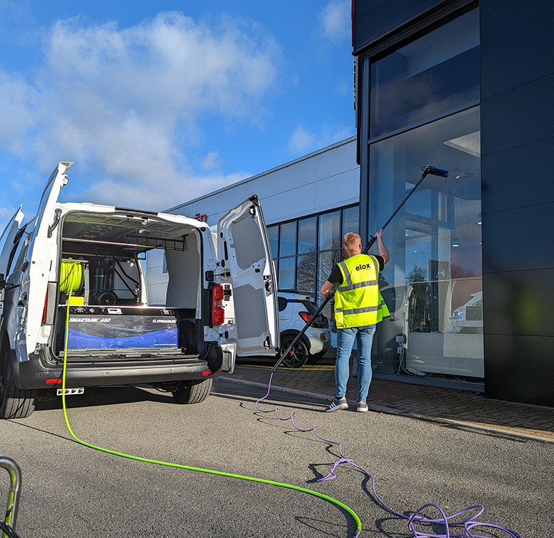 Homme nettoyant le vitrage d'un bâtiment à l'aide d'une perche et d'un nettoyeur haute pression installé dans un camion.