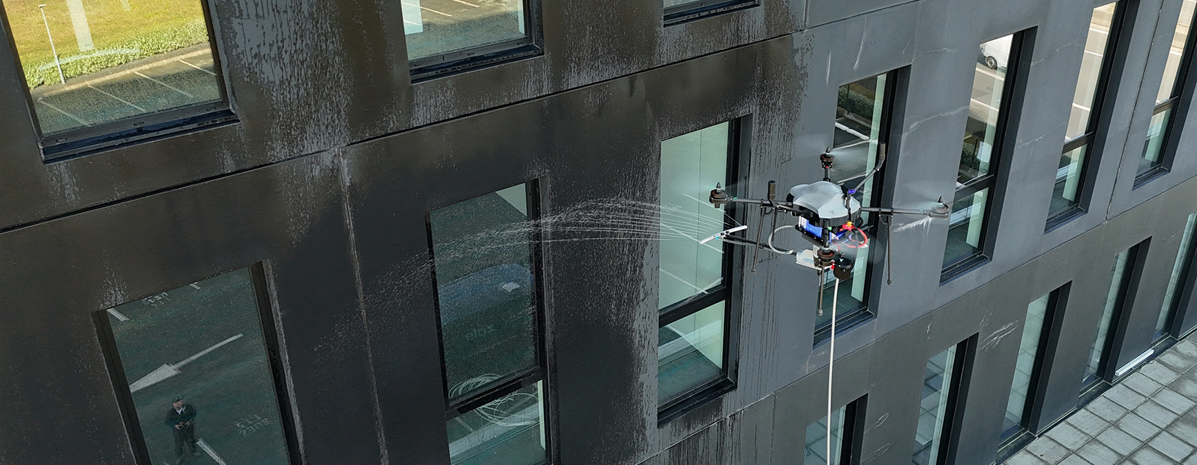 Drone nettoyant une facade noire et de vitrage.